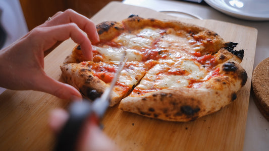 Slicing cheesy pizza - The Woodfired Co